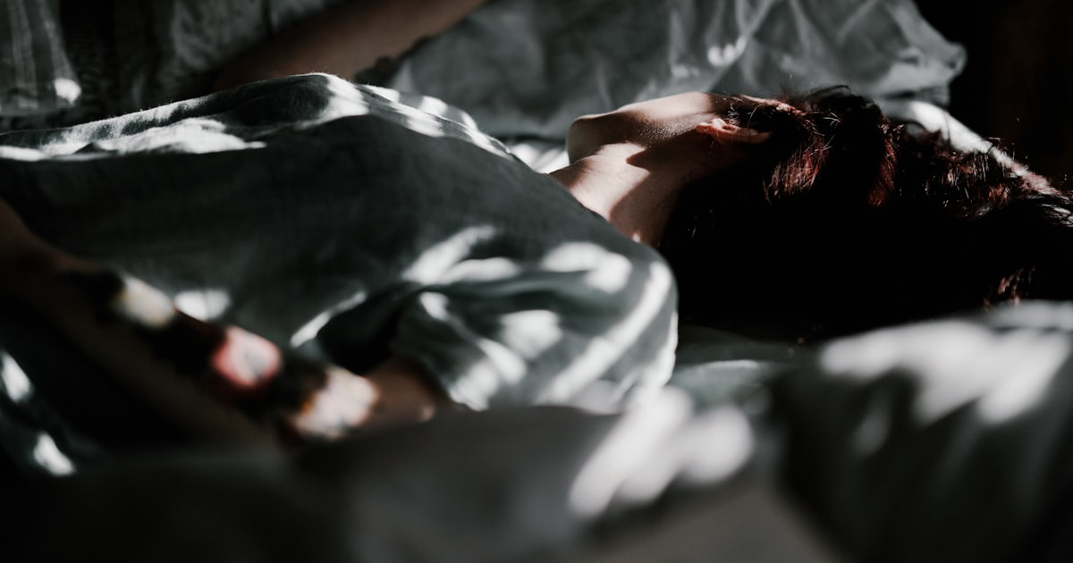 Person resting in bed under a blanket with morning light