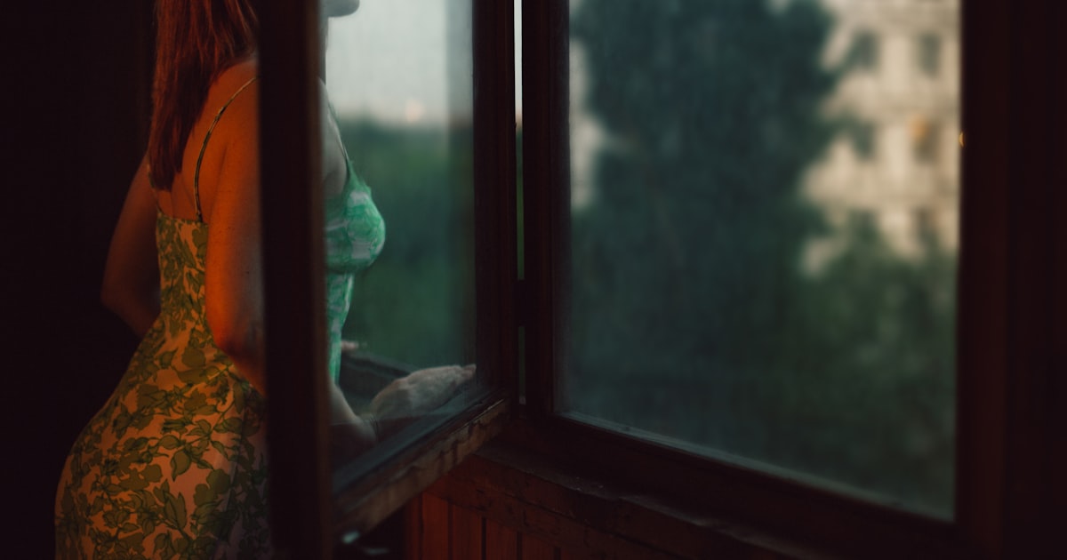 A woman leaning against a window, looking out