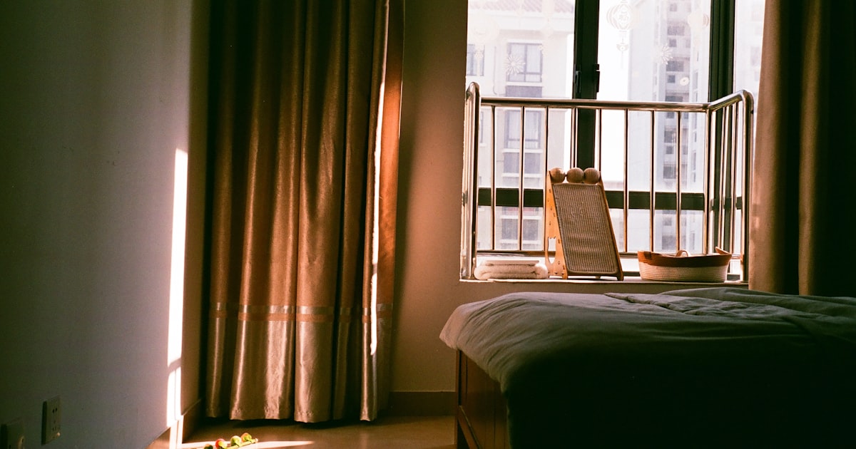 A bedroom with morning sunlight streaming through the window curtains